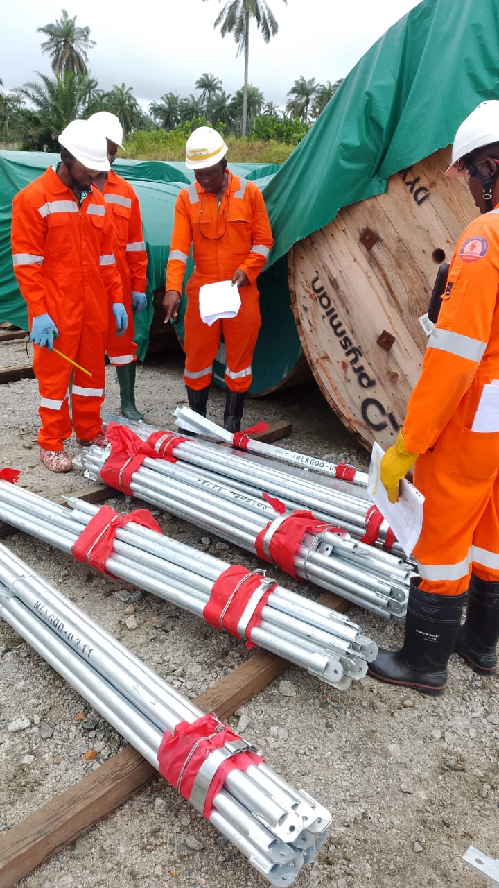 Workers in orange overalls inspecting bundled galvanised mast sections beside a cable drum