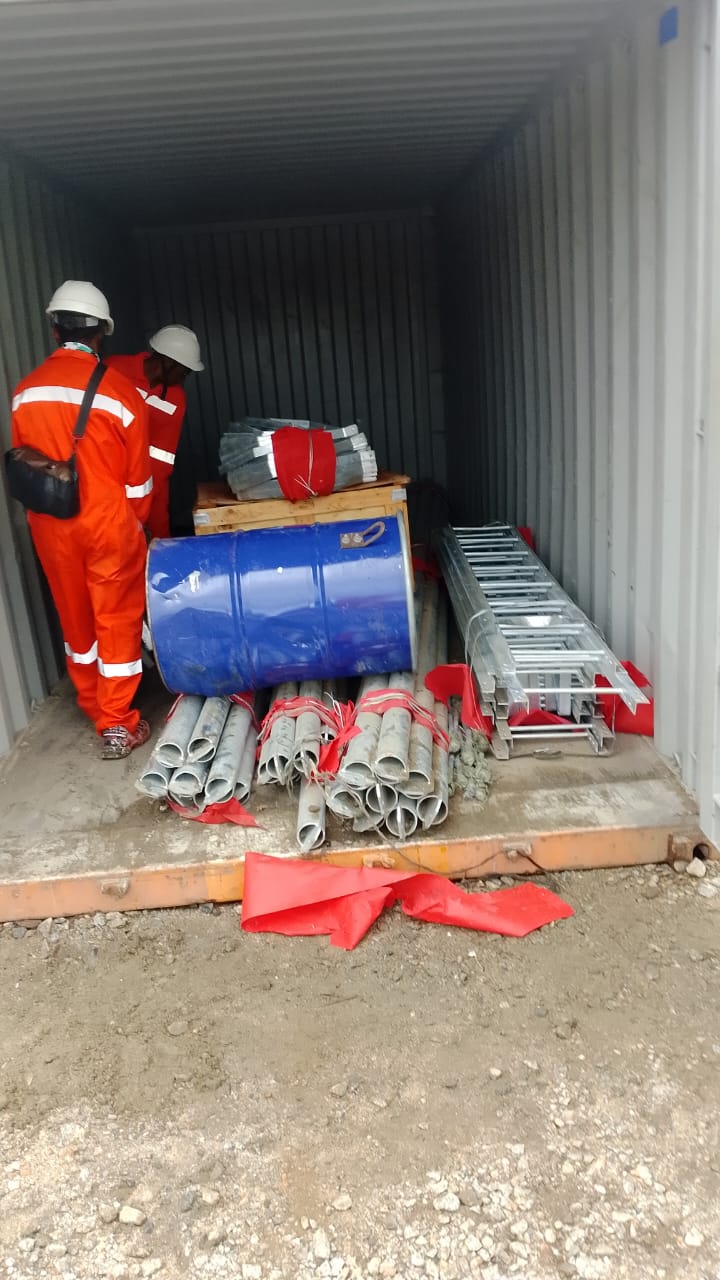 Workers loading galvanised steel pipes and ladders into a shipping container